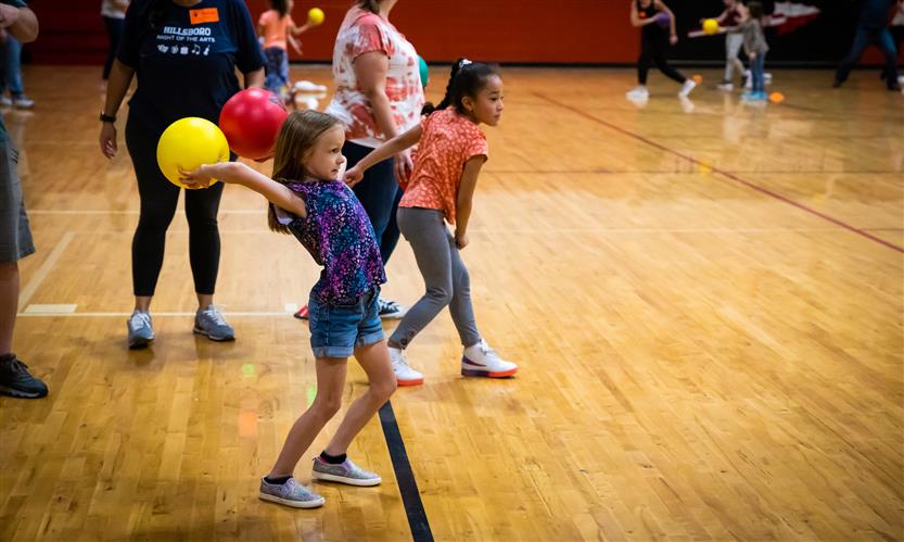 A girl with long hair throws two balls during a game of dodgeball.